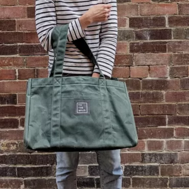 To the Wild Waxed Canvas Bag in green - against a brick wall